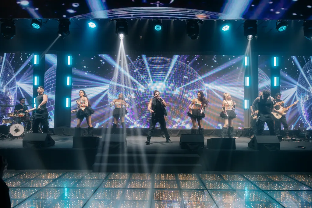 Palco azul com globo espelhado e o grupo inteiro em coreografia