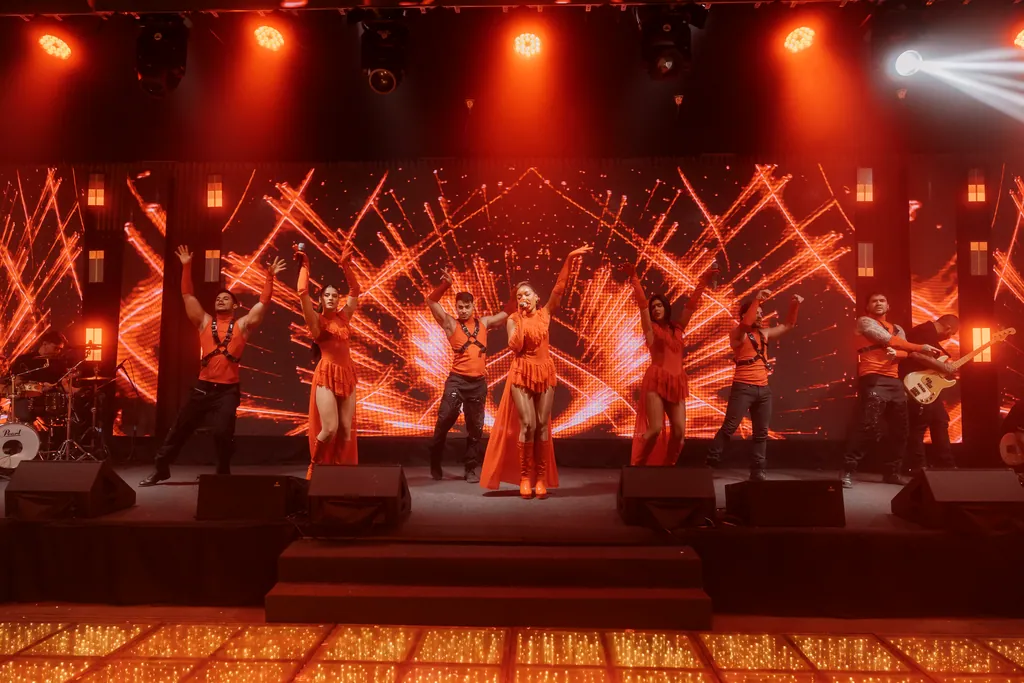 Palco inteiro aceso em vermelho, com feixes de luz e todo o grupo em cena