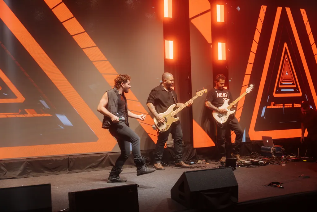 Músicos com guitarra e baixo em cena, triângulos laranja no LED