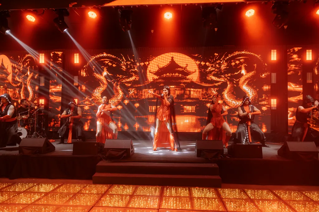 Grupo inteiro em cena no palco vermelho, cenário oriental em LED ao fundo